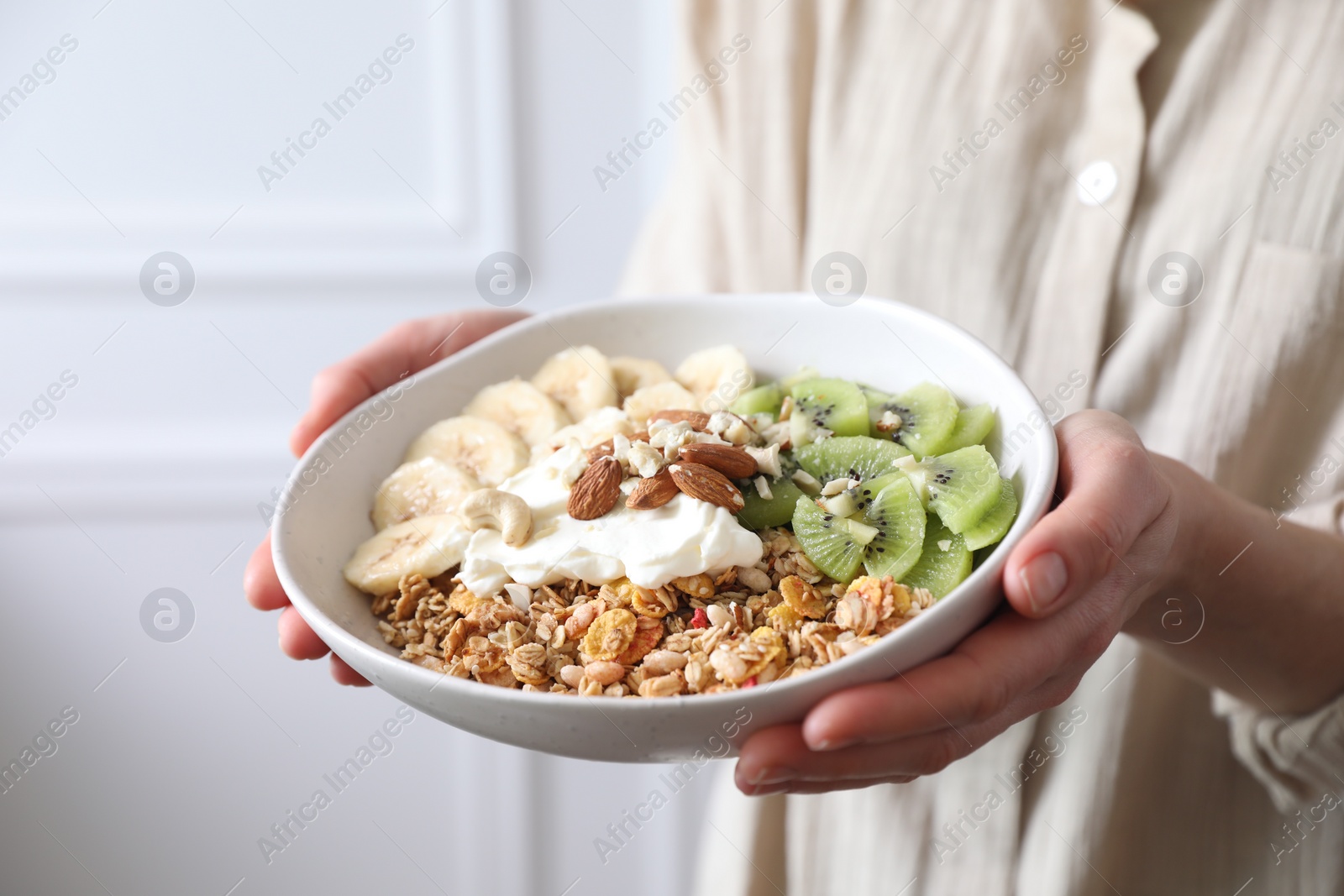 Photo of Woman holding bowl of tasty granola indoors, closeup