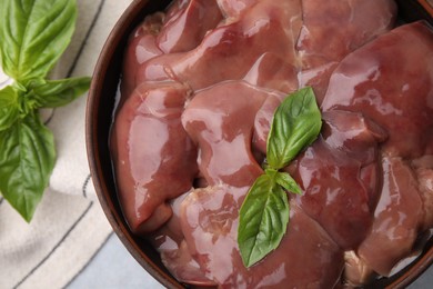 Bowl with raw chicken liver and basil on light grey table, flat lay