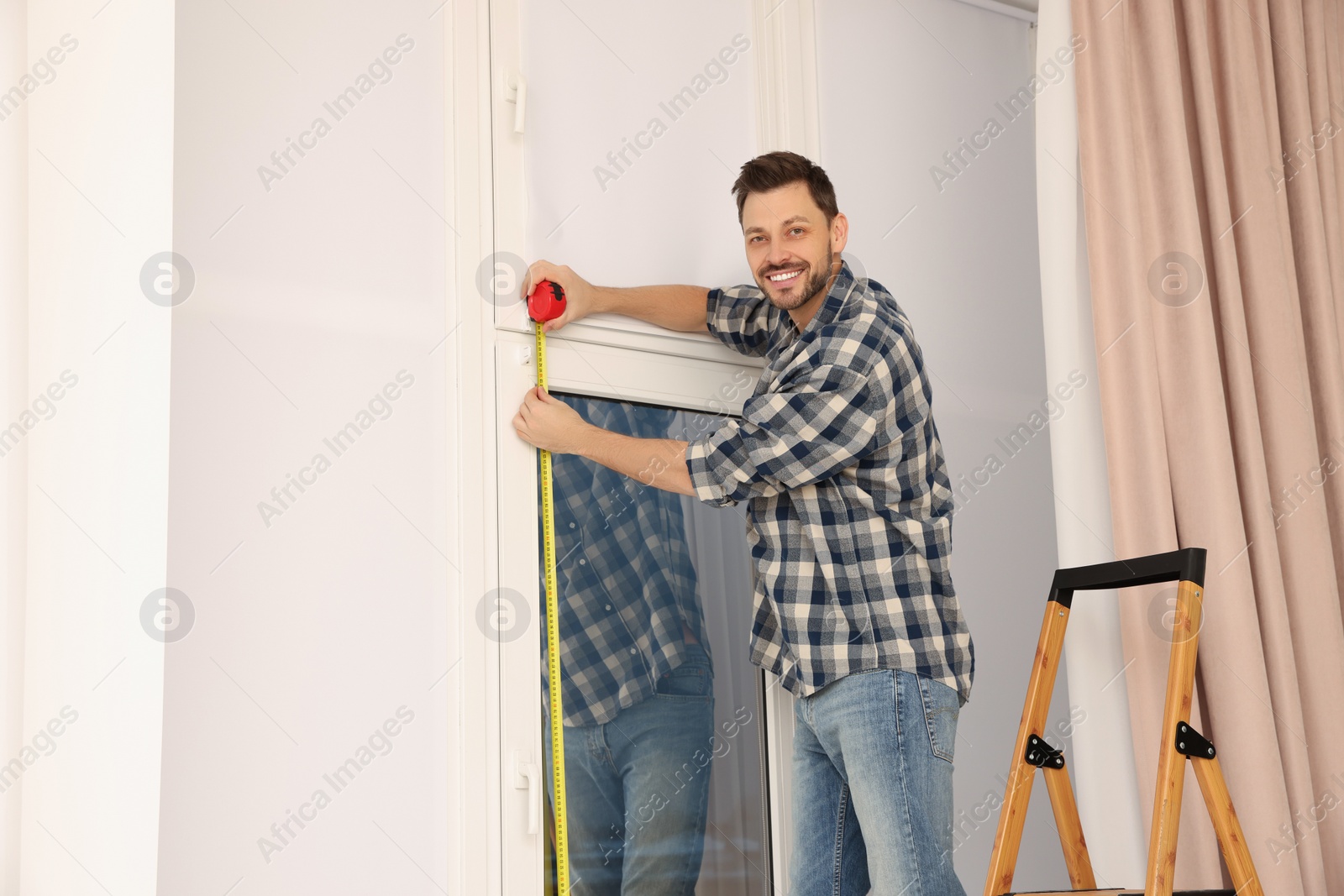 Photo of Man measuring window with tape indoors. Roller blinds installation