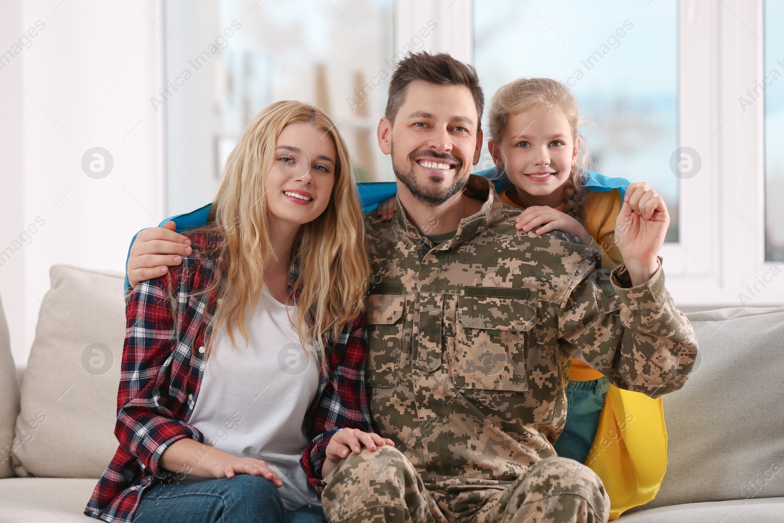 Photo of Soldier in military uniform reunited with his family and Ukrainian flag on sofa at home