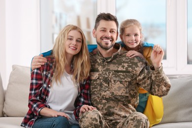 Soldier in military uniform reunited with his family and Ukrainian flag on sofa at home