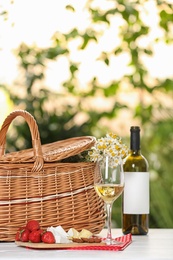 Picnic basket and wine with products on table against blurred background, space for text