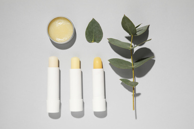 Photo of Hygienic lipsticks and eucalyptus on light grey background, flat lay