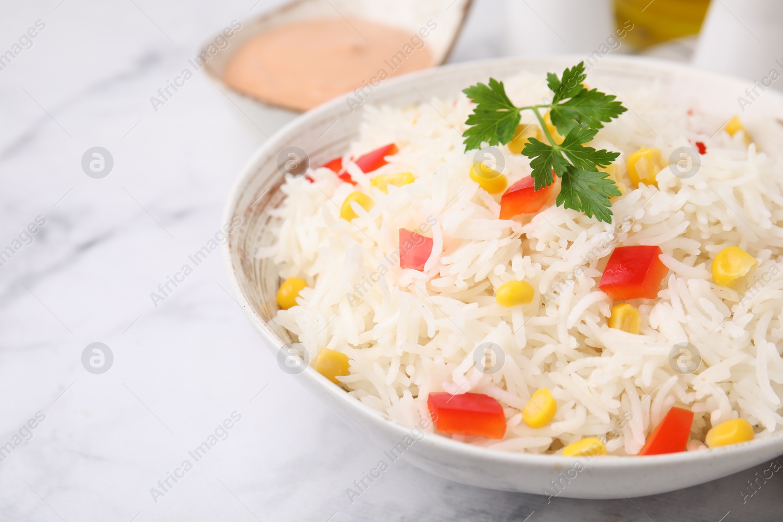 Photo of Bowl of delicious rice with vegetables and parsley on light table, closeup