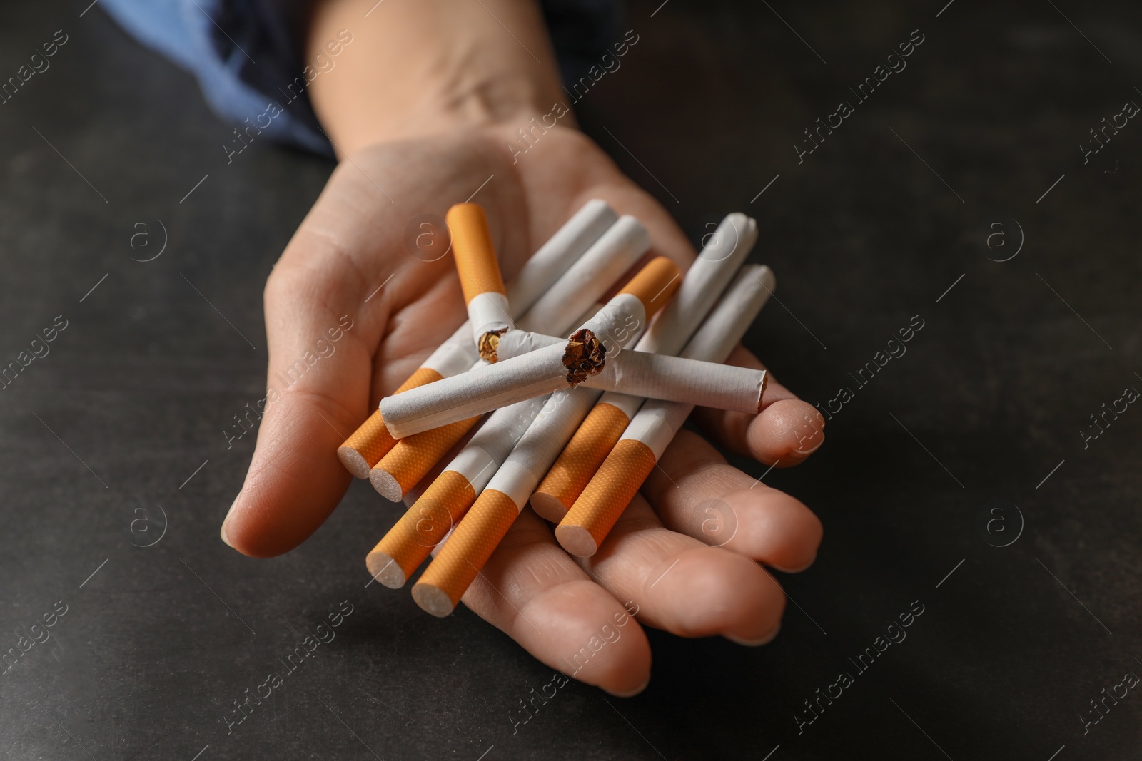 Photo of Stop smoking. Woman holding whole and broken cigarettes at black table, closeup