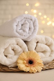 Photo of Rolled terry towels and flower on white table near brick wall indoors