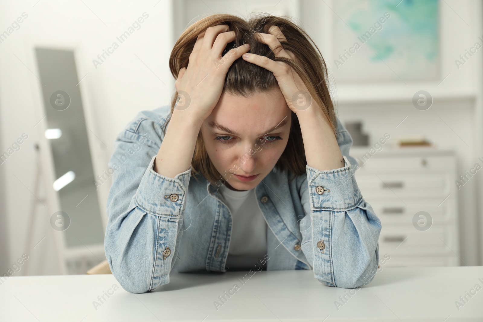 Photo of Sad young woman sitting at white table in room