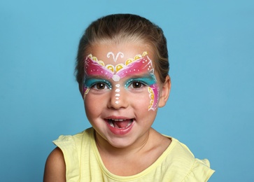 Photo of Cute little girl with face painting on blue background