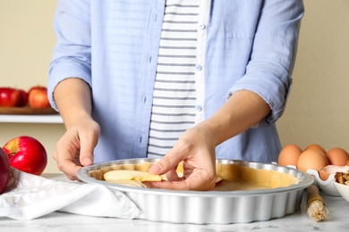 Woman putting apple slice into baking dish with dough to make traditional English pie at table, closeup