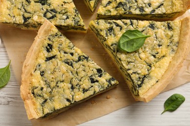 Cut delicious spinach pie on white wooden table, flat lay