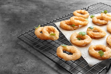 Cooling rack with fried onion rings on grey background