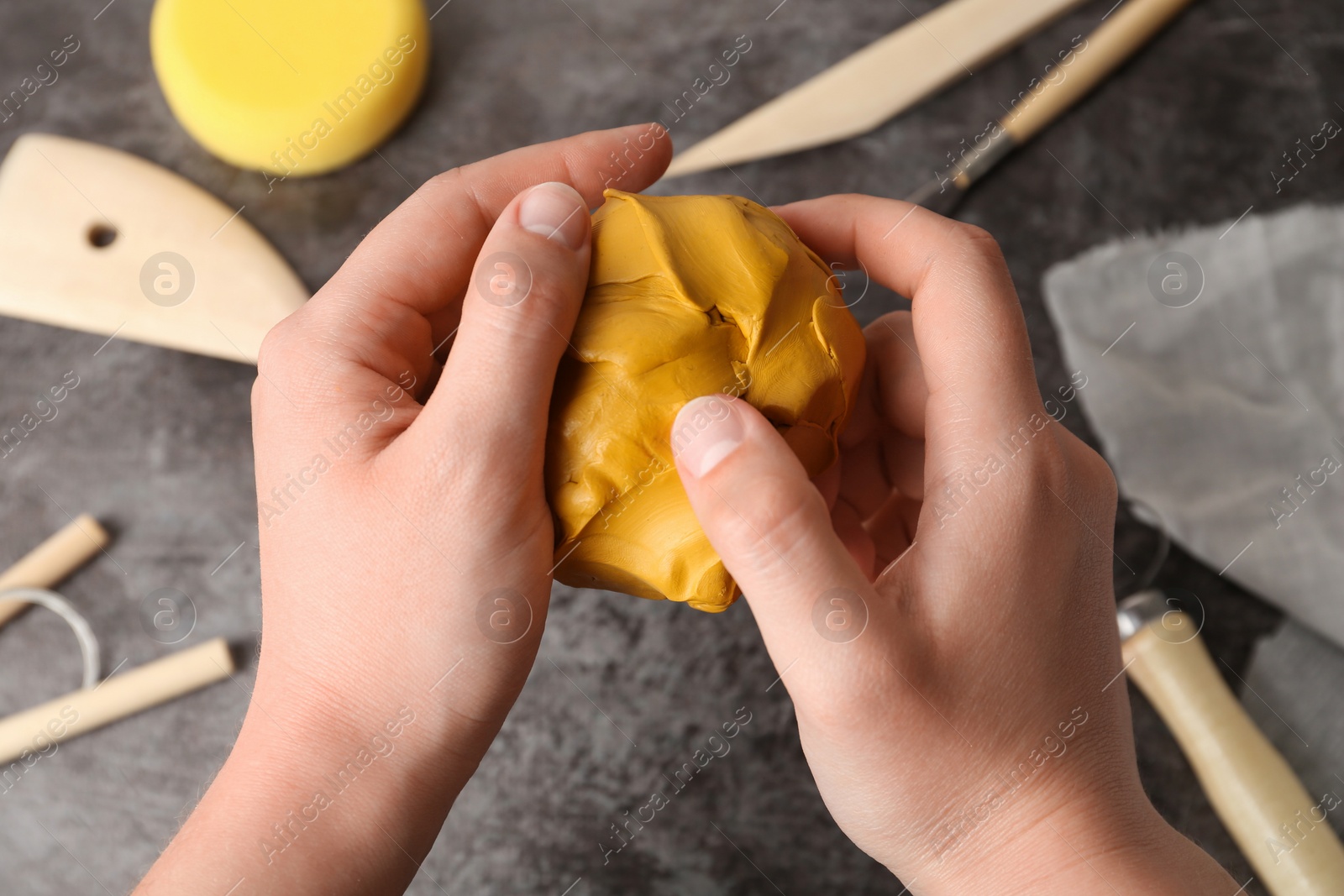 Photo of Woman holding clay over grey stone table with modeling tools, closeup