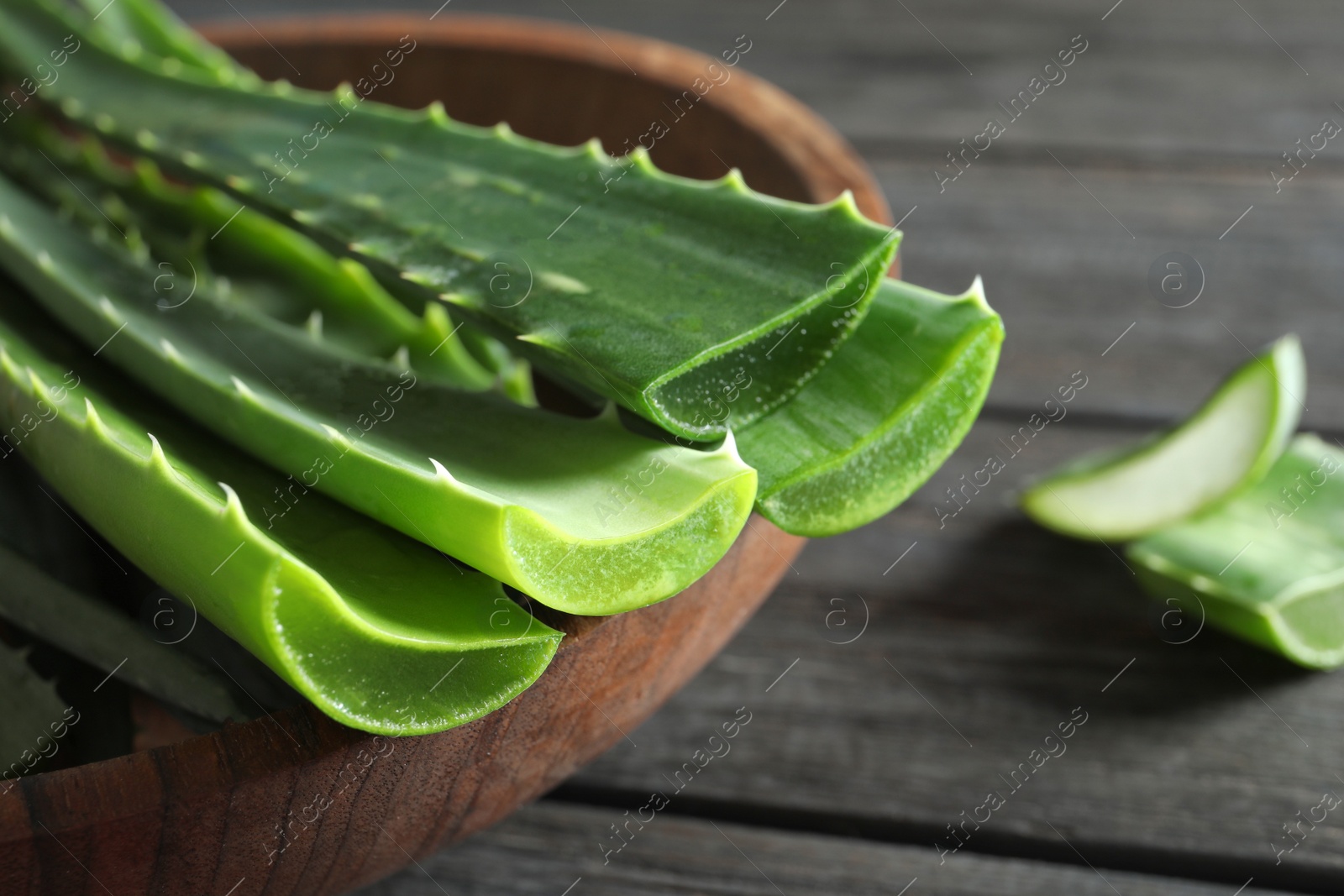 Photo of Bowl with fresh aloe vera leaves on wooden table, closeup