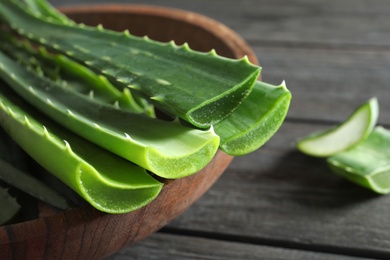 Bowl with fresh aloe vera leaves on wooden table, closeup