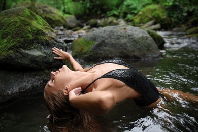 Photo of Beautiful young woman relaxing in mountain river near rock outdoors