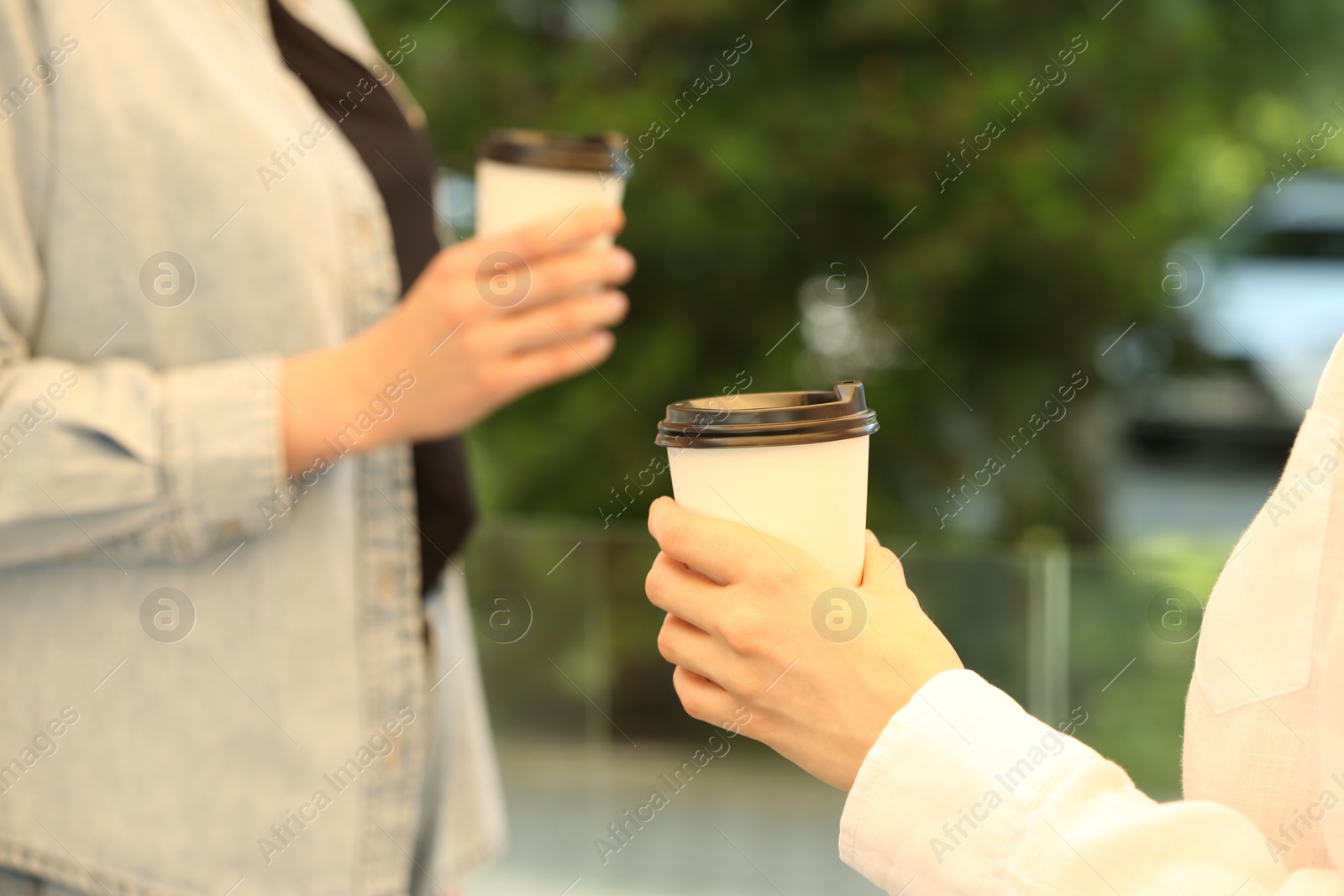 Photo of Women holding takeaway paper cups outdoors, closeup. Coffee to go