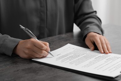 Photo of Woman signing document at dark table indoors, closeup