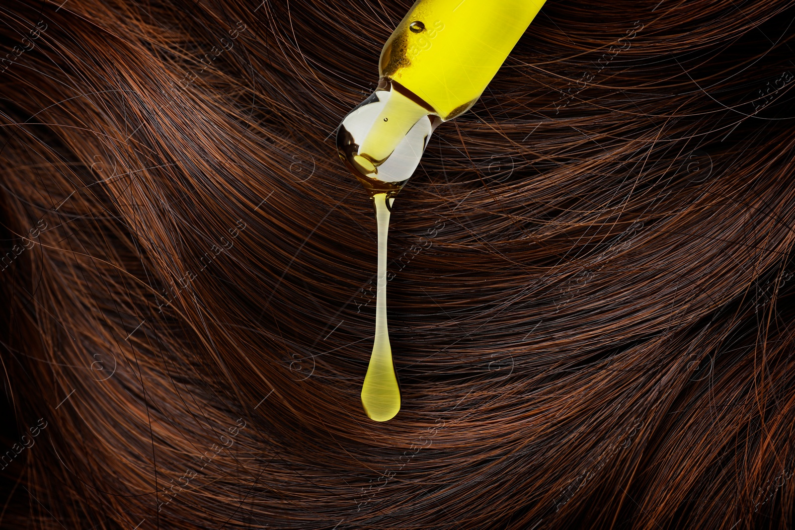 Image of Dripping cosmetic oil from pipette onto brown hair, closeup