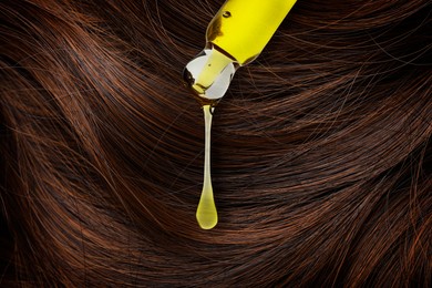 Dripping cosmetic oil from pipette onto brown hair, closeup