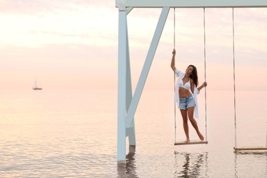 Photo of Young woman enjoying sunrise on swing over water