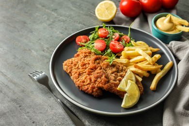 Tasty schnitzels served with potato fries, tomatoes and arugula on grey table, closeup