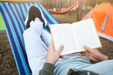 Photo of Man with book resting in comfortable hammock outdoors, closeup