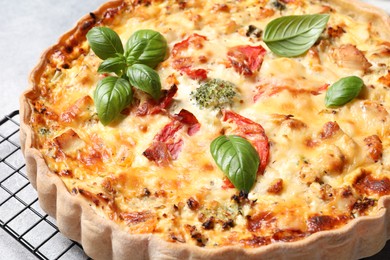 Photo of Tasty quiche with tomatoes, basil and cheese on light textured table, closeup