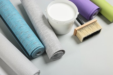 Different wallpaper rolls, brush and bucket with glue on light background