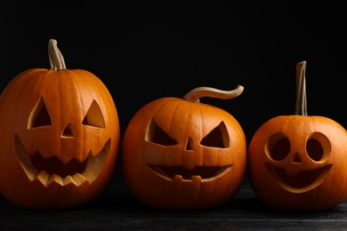 Scary jack o'lanterns made of pumpkins on wooden table against black background. Halloween traditional decor