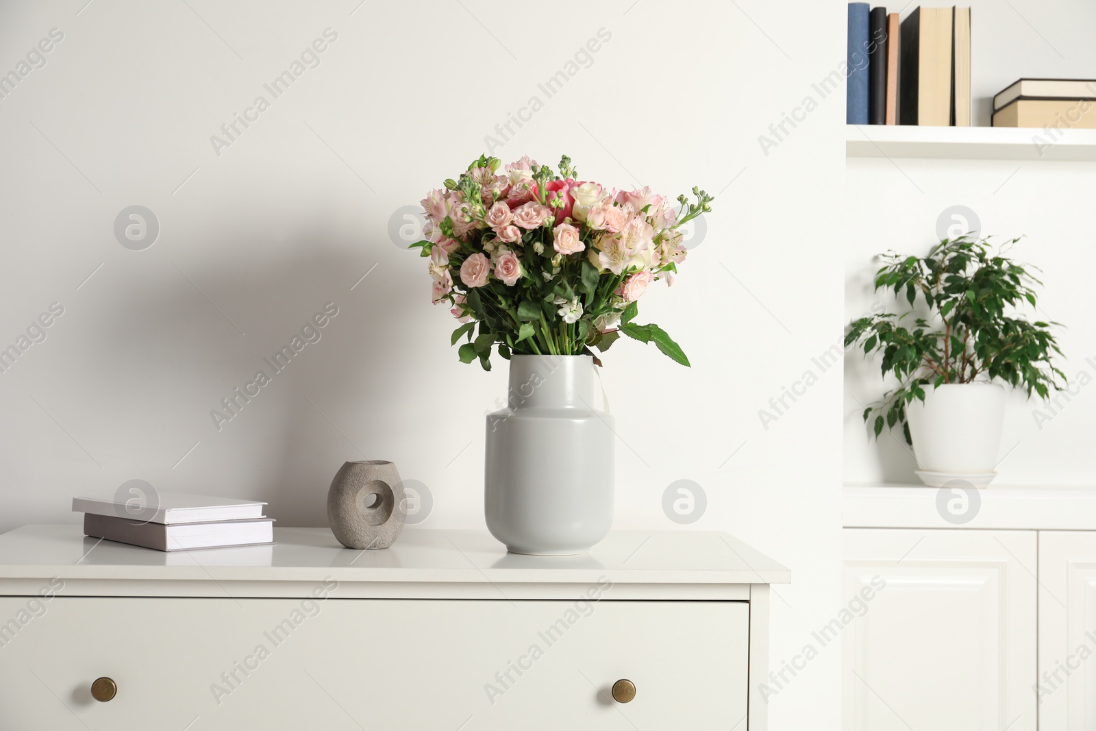 Photo of Beautiful bouquet of fresh flowers in vase on chest of drawer indoors