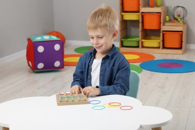 Photo of Motor skills development. Boy playing with geoboard and rubber bands at white table in room