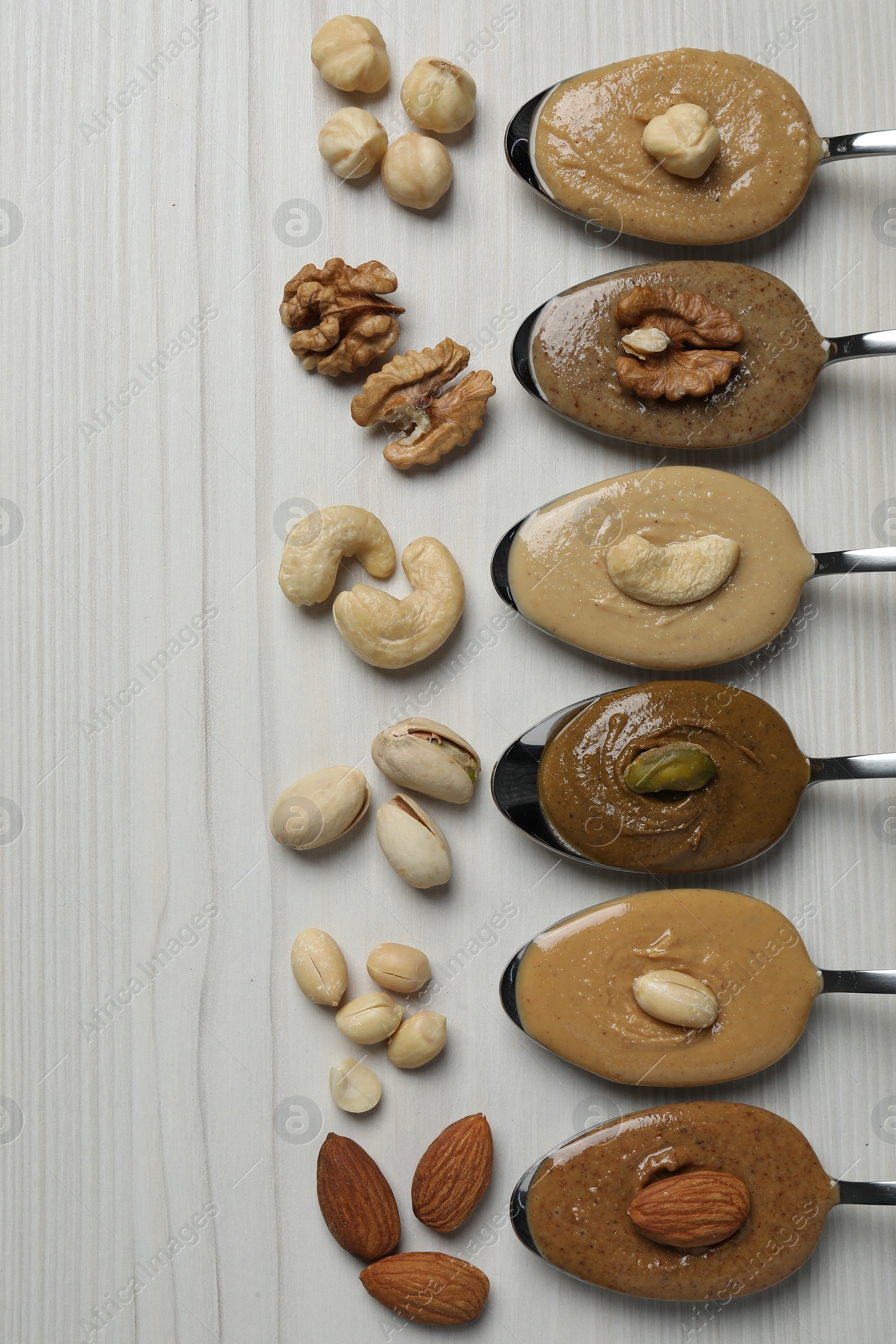 Photo of Tasty nut butters in spoons and raw nuts on white wooden table, flat lay