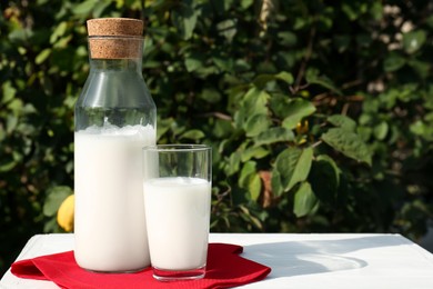 Photo of Glass and bottle of fresh milk on white wooden table outdoors. Space for text