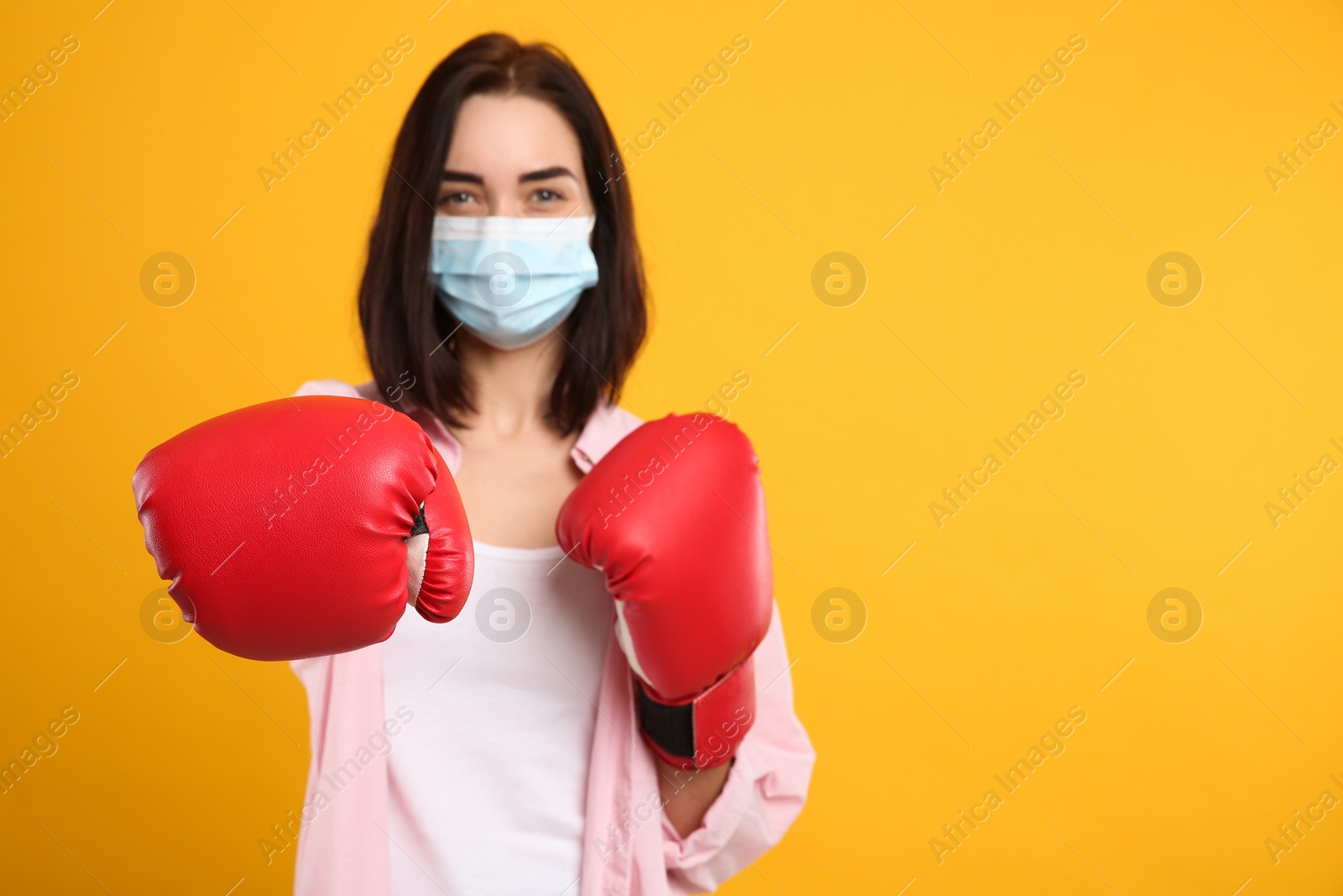 Photo of Woman with protective mask and boxing gloves on yellow background, space for text. Strong immunity concept