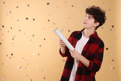 Photo of Happy teenage boy blowing up party popper on light brown background