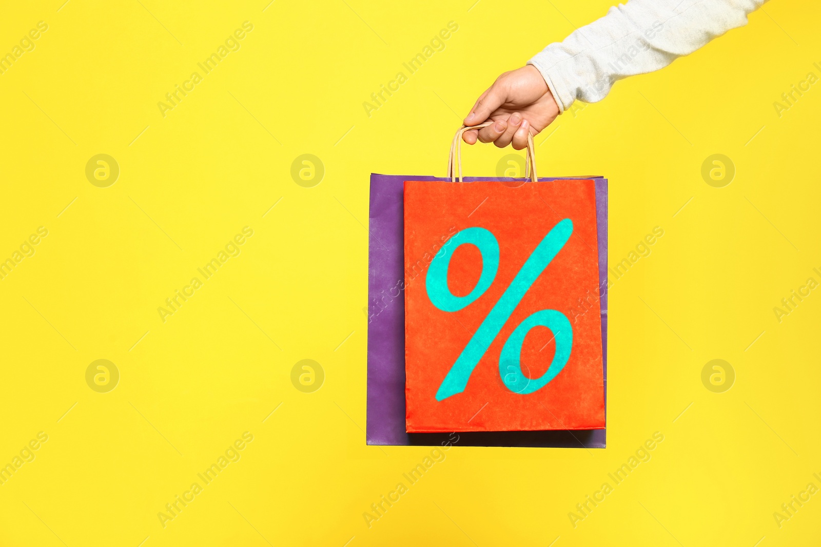 Image of Man holding paper shopping bag with percent sign on yellow background, closeup. Discount concept