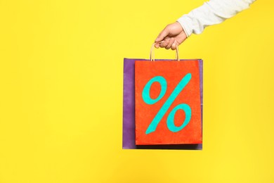 Image of Man holding paper shopping bag with percent sign on yellow background, closeup. Discount concept