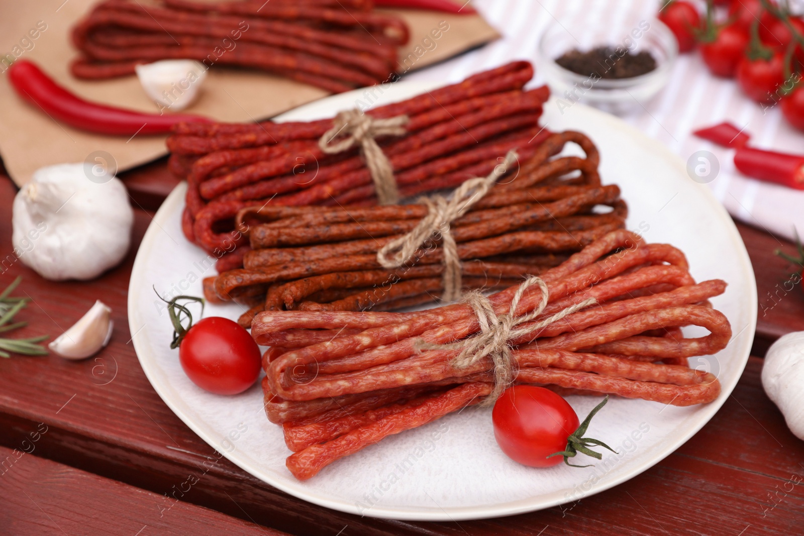 Photo of Bundles of delicious kabanosy with tomatoes on wooden table