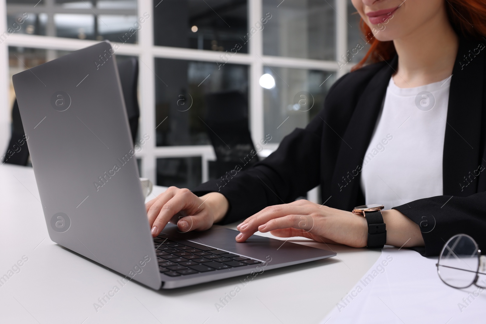 Photo of Woman working with laptop at white desk in office, closeup