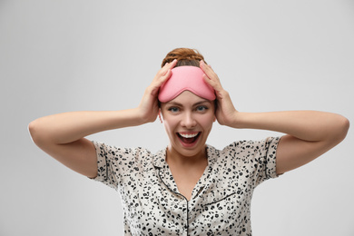 Photo of Beautiful woman wearing pajamas and sleeping mask on light grey background. Bedtime