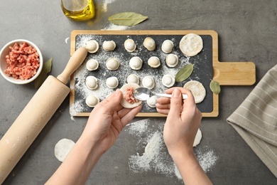 Woman cooking delicious dumplings over grey table, top view