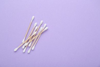 Wooden cotton buds on violet background, flat lay. Space for text