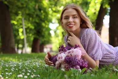 Beautiful woman with bouquet of spring flowers on green grass in park, space for text