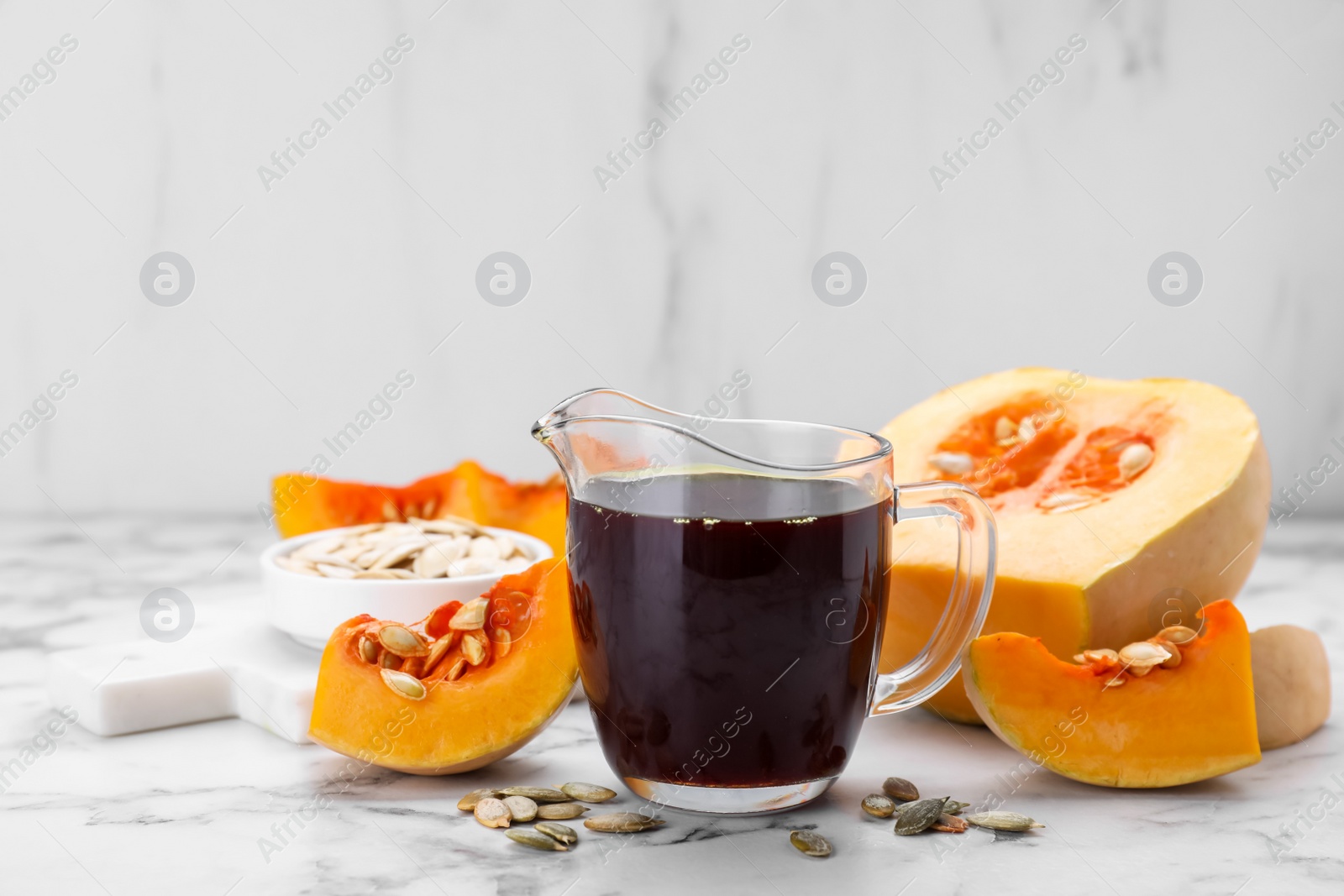 Photo of Fresh pumpkin seed oil in glass pitcher on white marble table. Space for text