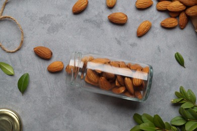 Photo of Jar with tasty almonds and green leaves on light grey table, flat lay