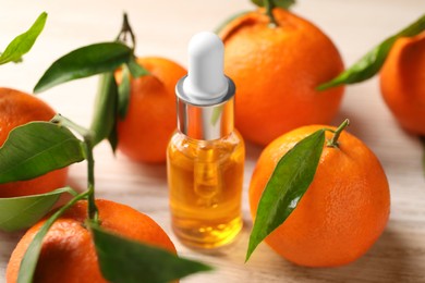 Bottle of tangerine essential oil and fresh fruits on white wooden table, closeup