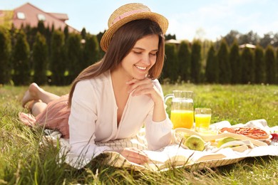 Photo of Young woman reading book on blanket outdoors. Summer picnic