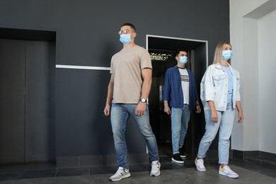 Photo of Group of people in face masks walking out from elevator. Protective measure