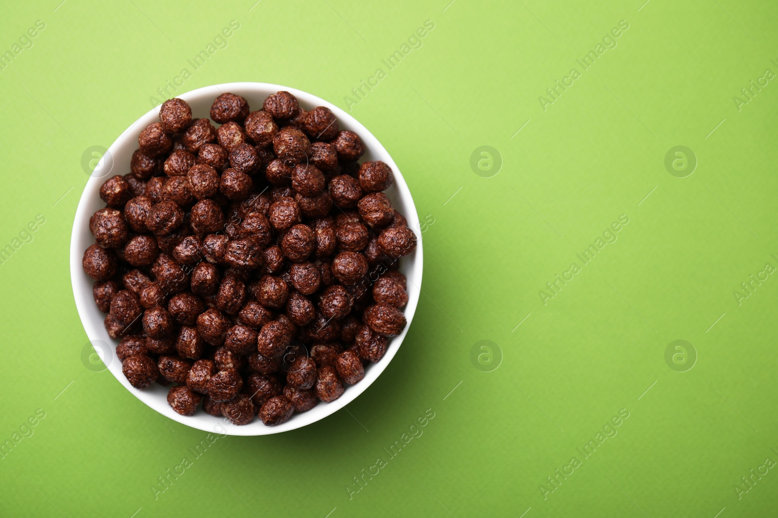 Photo of Chocolate cereal balls in bowl on green table, top view. Space for text