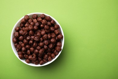 Photo of Chocolate cereal balls in bowl on green table, top view. Space for text